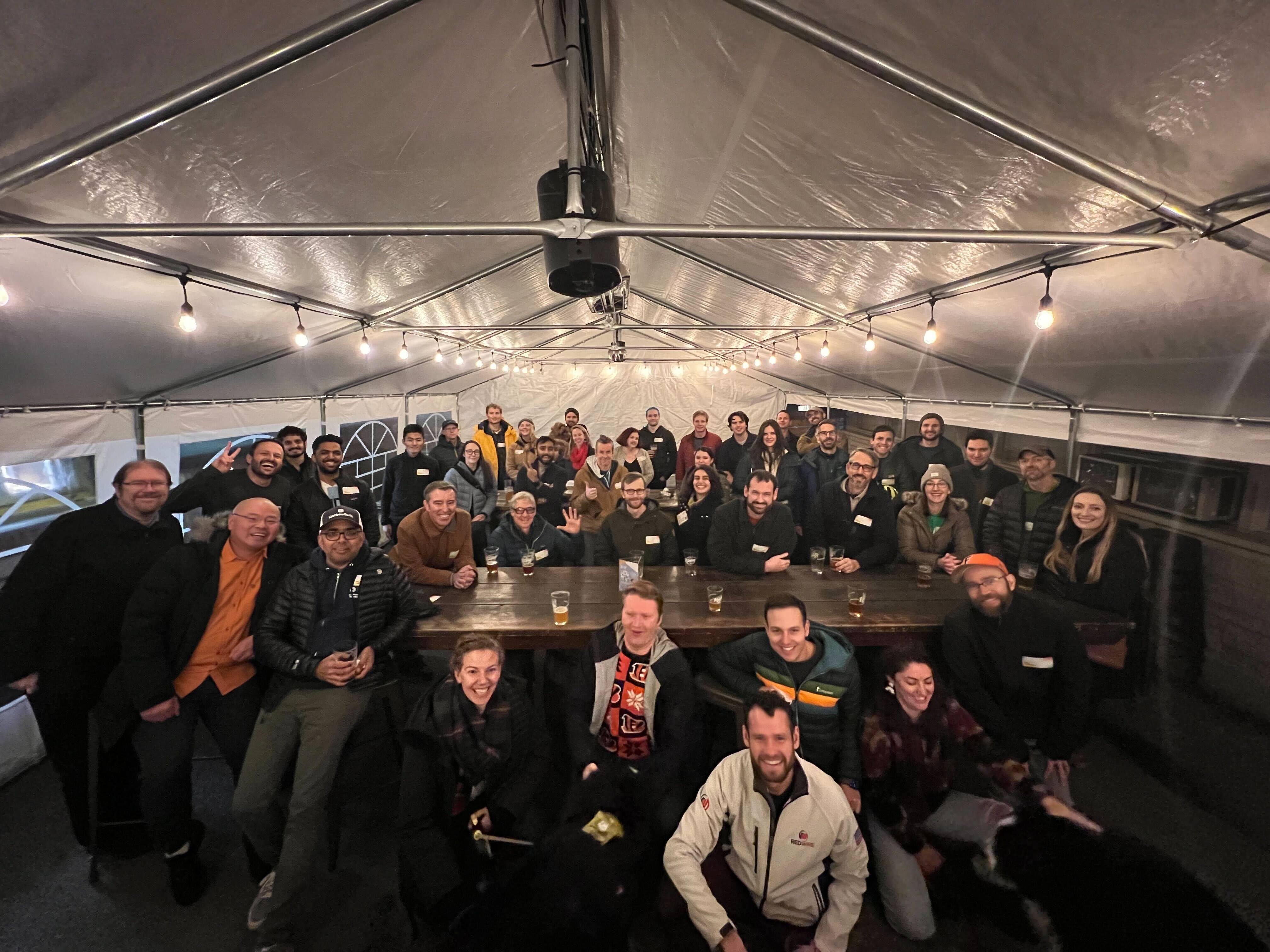 Large group of people beneath a large tarp with string lights smiling and looking at the camera.
